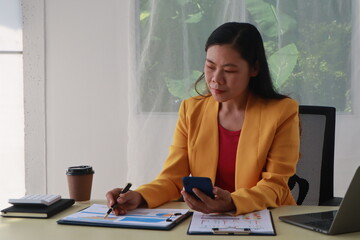 A middle-aged businesswoman in a yellow suit works at a desk on tips for financial stability. She...
