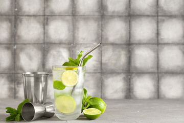 Glass of fresh Mojito cocktail with limes and mint on grey table