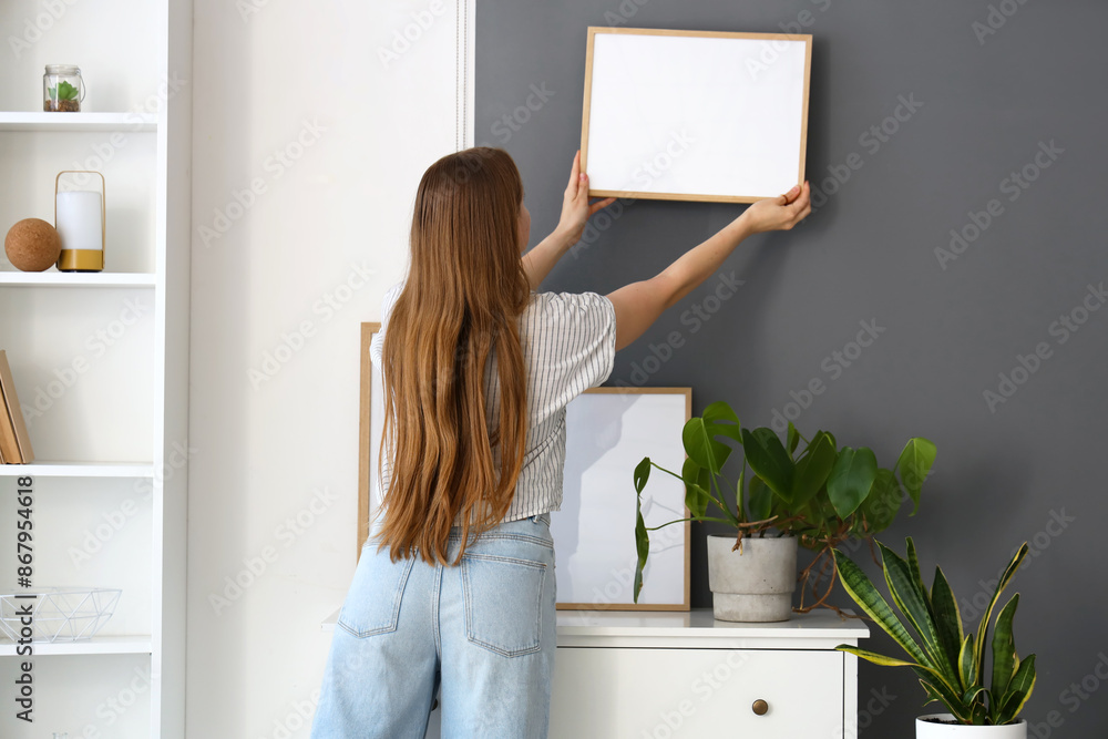 Canvas Prints Young woman hanging frame on wall at home