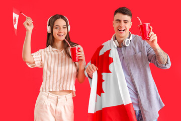 Young couple with flags of Canada and soda on red background