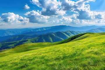 Naklejka premium Panoramic view of lush green grassy hills and majestic mountain range under bright blue sky with fluffy white clouds. Scenic landscape of nature, perfect for hiking, travel, and adventure.