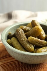 Pickled cucumbers in bowl on wooden board, closeup
