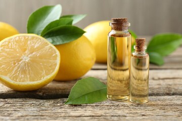 Essential oils in bottles, lemons and green leaves on wooden table