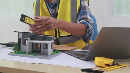 A male engineer inspects a structural model of a house at his workstation, ensuring compliance with design specifications and safety standards.