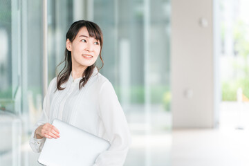 ビルの前でノートパソコンを持つビジネスウーマン(士業・行政書士・司法書士・中小企業診断士)