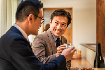 居酒屋・飲み屋のカウンターで部下と楽しくお酒を飲むビジネスマンの男性
