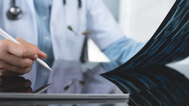 Orthopedics surgeon doctor using digital tablet and examining and recording patient's knee joint x-ray films, MRI bone, ct scan at radiology orthopedic unit in hospital. knee joint film x ray