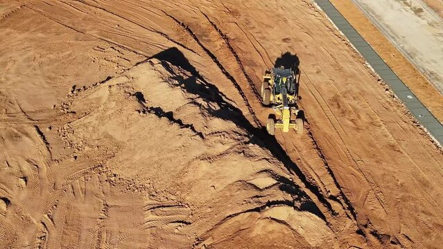 Front on aerial view of a grader moving along amongst piles of dirt
