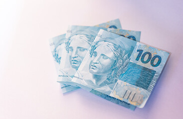 Notas do Real Brasileiro em fundo branco. Fotografia com ângulo fechado. Economia do Brasil. Notas de 100 reais. Notas dobradas. VIsta superior.