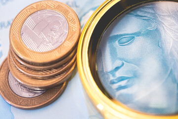 Nota de 100 reais com uma pilha de moedas de 1 Real em fotografia closeup. Crise financeira e juros altos no Brasil. Real Brasileiro, moeda corrente do Brasil.