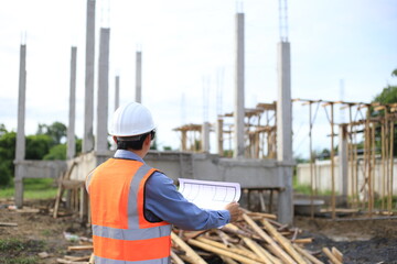 Fototapeta premium Young professional engineer in hat and blueprint paper is working...At the house construction site. Motivation: success, career growth. achieving goals