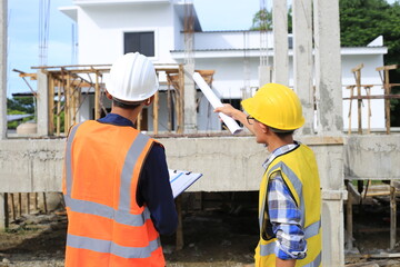 Young professional engineer in hat and blueprint paper is working...At the house construction site....