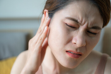Asian woman having an earache problem. An earache is sharp, dull, or burning ear pain in one or both ears.