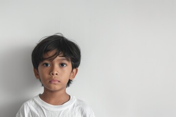 Young boy with serious expression standing against a plain white background