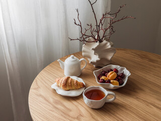 Tea party set table - tea, croissant, fruits and berries on a round wooden table