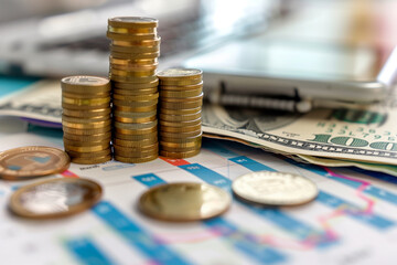 stack of coins and a stack of dollar bills sit on top of a piece of paper with graphs