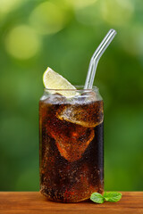 glass of cold cola with ice cubes or cuba libre cocktail on wooden table outdoors
