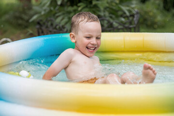 It's a hot day. A cute boy is swimming and splashing in the pool. A happy little boy smiles at the camera. Splashes of water are flying in all directions. The concept of summer holidays with children.