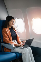 Professional woman working on a laptop while seated in an airplane cabin, showcasing modern business travel and productivity during flights.