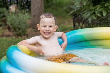 It's a hot day. A cute boy is swimming and splashing in the pool. A happy little boy smiles at the camera. Splashes of water are flying in all directions. The concept of summer holidays with children.