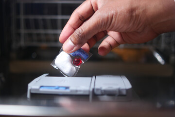 The person is using a soap dispenser for the dishwasher with their hand