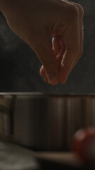 vertical shot man adding salt to boiling water in saucepan