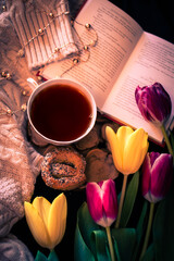 A hot cup of tea with a book, cookie, and flowers.