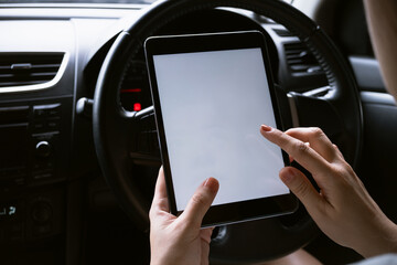 Woman sitting in a car and holding a tablet with blank screen.