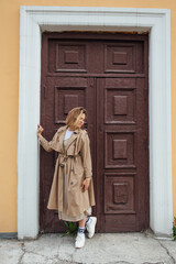 Obraz premium Young millennial woman with wild hair dressed in an autumn coat posing near the door of an old building.