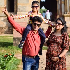 Indian couple posing for maternity baby shoot with their 5 year old kid. The couple is posing in a lawn with green grass and the woman is flaunting her baby bump in Lodhi Garden in New Delhi, India