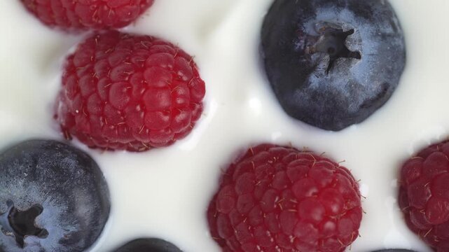 Slow motion of white yogurt with raspberry and blueberry, top view, rotation. Sour cream or fresh greek yogurt.
