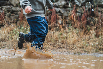 A young boy is running through a puddle of water