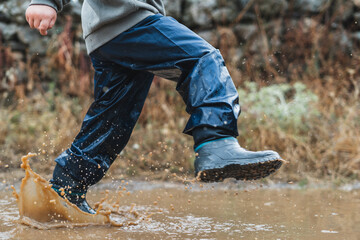 A young boy is running through a puddle of water in his rain boots