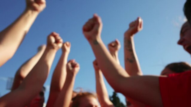 out of focus arms raised celebration. Close-up of female rugby players joining hands in a show of team spirit and unity, wearing red jerseys.