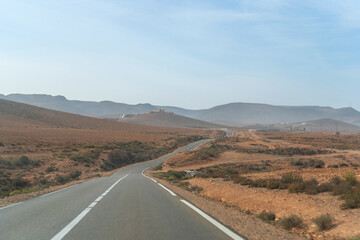 Winding road through Moroccan landscape, arid terrain, distant hills, sparse vegetation, rural area