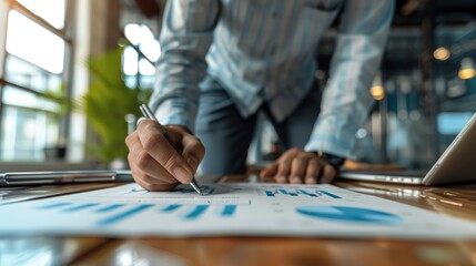 Obraz premium A businessman working on a desk, analyzing financial graphs and charts with a pen.