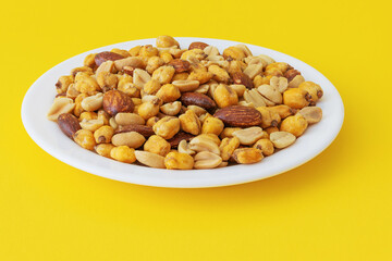 Roasted peanuts, corn and almonds in a plate on a yellow background