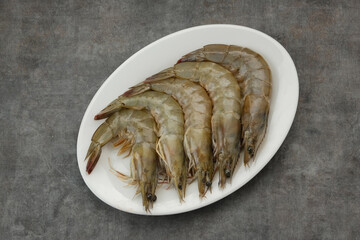 Fresh shrimps served on white plate with dark background, food preparation.
