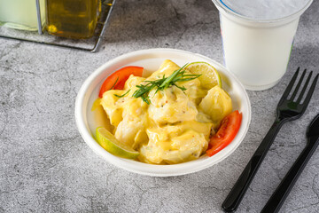 Potato salad with tomatoes and lemon on gray stone table