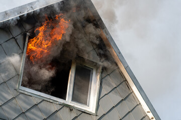 Flames and smoke coming out of the window of a burning wooden house