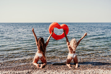 Two women are on a beach holding a red heart shaped float