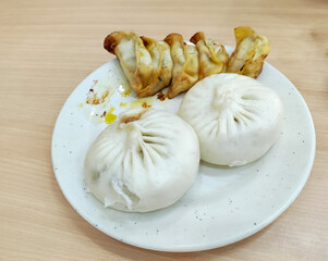 two white steamed stuffed bun and fried dumplings on the white plate for eating