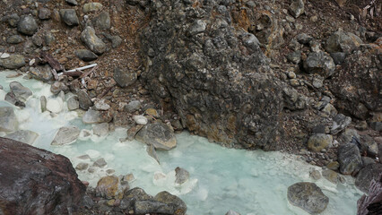 A clear river with hot sulfur water flows through the rugged landscape of the Sorikmarapi volcano area, North Sumatra, Indonesia.