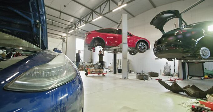 Mechanics performing maintenance and repairs on electric vehicles in a well-equipped modern automotive workshop. Vehicles lifted on hoists for inspection. EV repair concept. Auto Service, Electric Car