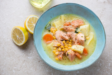 Chowder with salmon served in a turquoise bowl, horizontal shot on a beige stone background,...