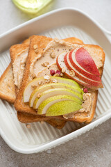 Toasts with peanut butter and fresh pear slices in a beige serving tray, vertical shot, middle close-up, selective focus