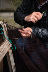 Hands of a sailor who is mending a fishing net. Vertical photo.