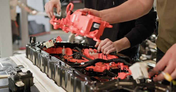 Two technicians are working on an electric car battery pack in a workshop. The image captures the detailed assembly and repair process. Electric car. Pack of battery cells module. EV car