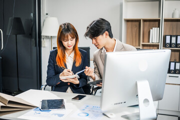  A businessman and businesswoman work late in the office, discussing strategies at a desk. They use technology and teamwork to plan and achieve success, demonstrating effective communication.