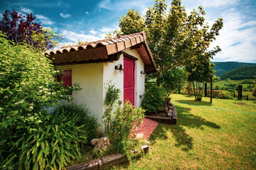 Cute cottage in a fairytale setting surrounded by trees, plants and flowers.